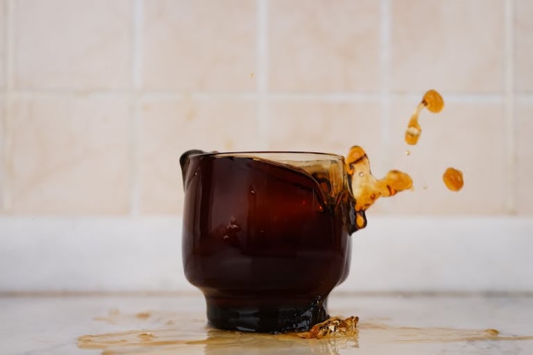 Brown glass cup with coffee splash against tiled background. Eye-catching spill captured mid-air.
