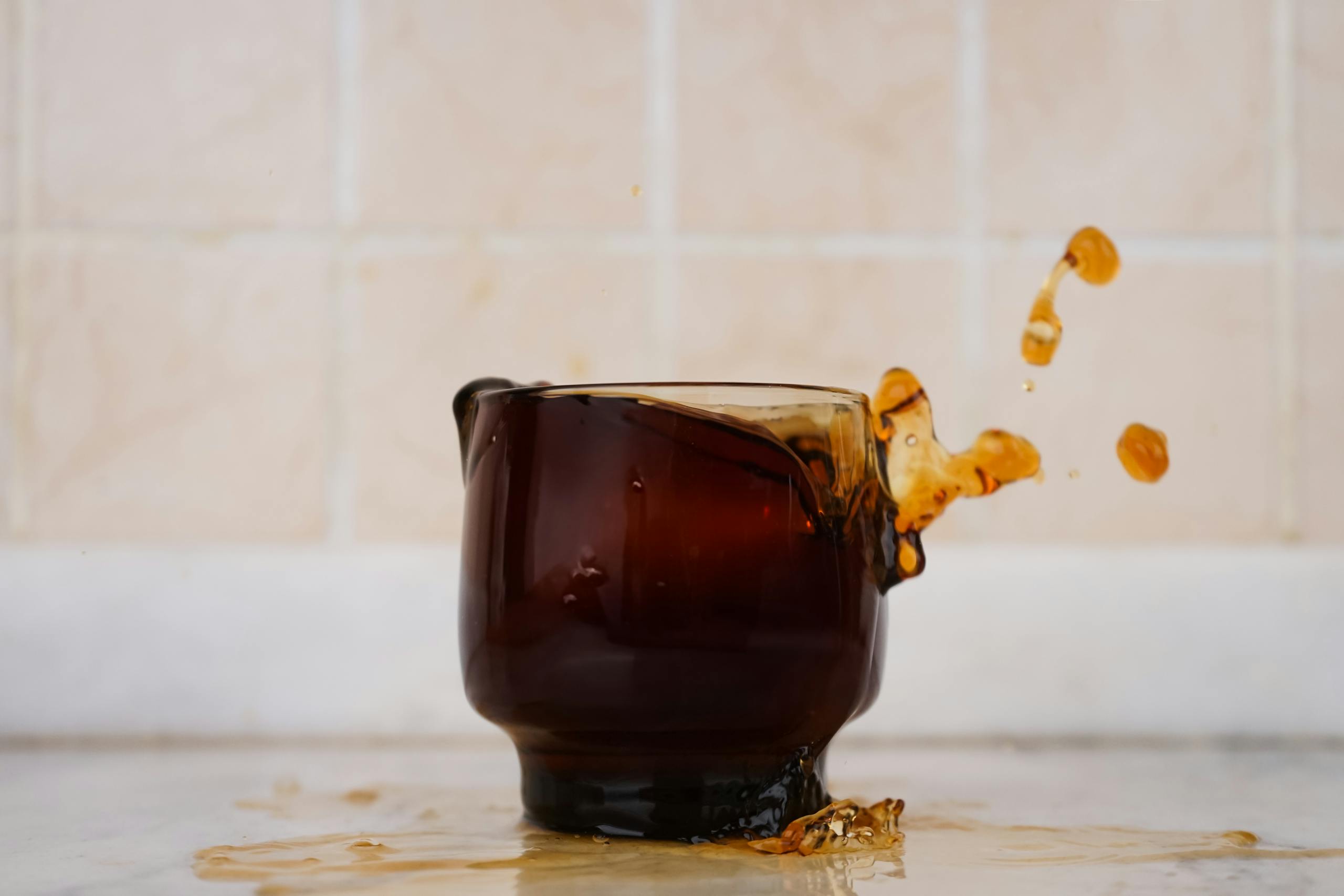 Brown glass cup with coffee splash against tiled background. Eye-catching spill captured mid-air.