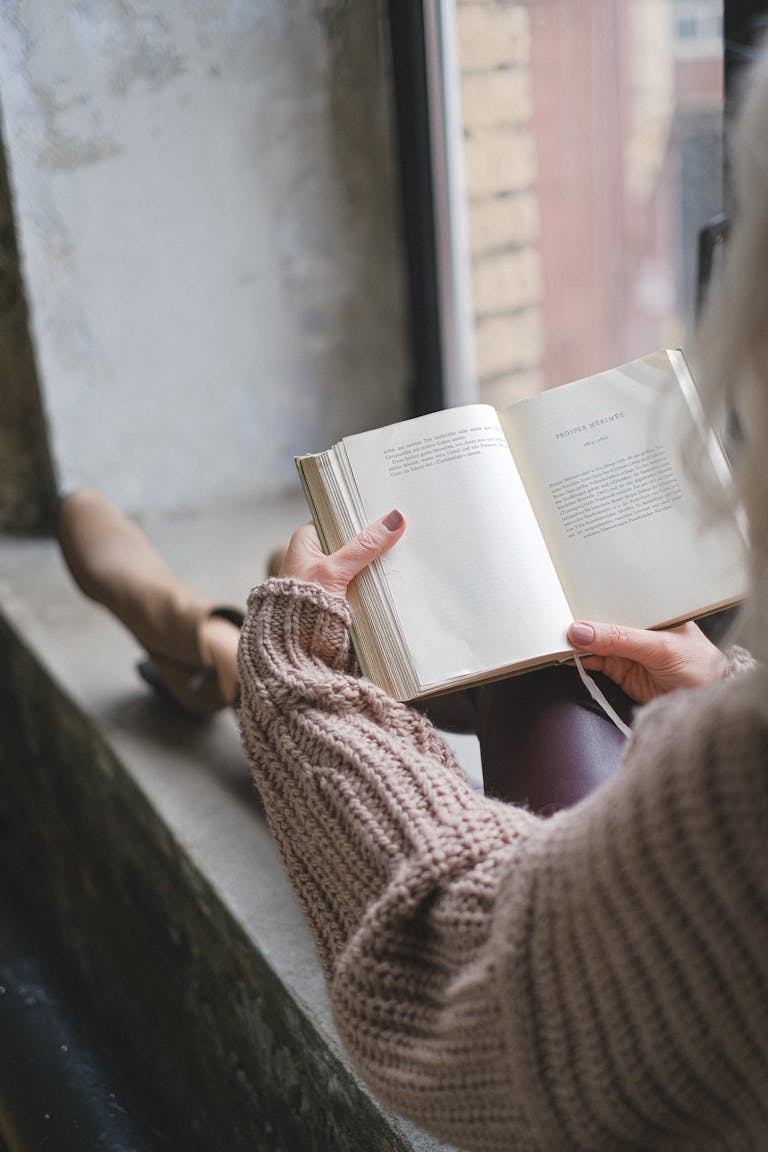 A person wearing a sweater reads by the window, enjoying a cozy fall morning.