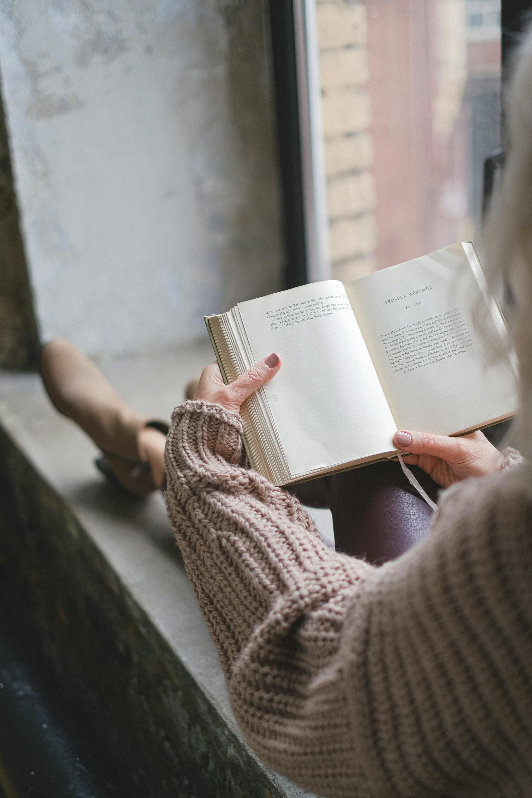 A person wearing a sweater reads by the window, enjoying a cozy fall morning.
