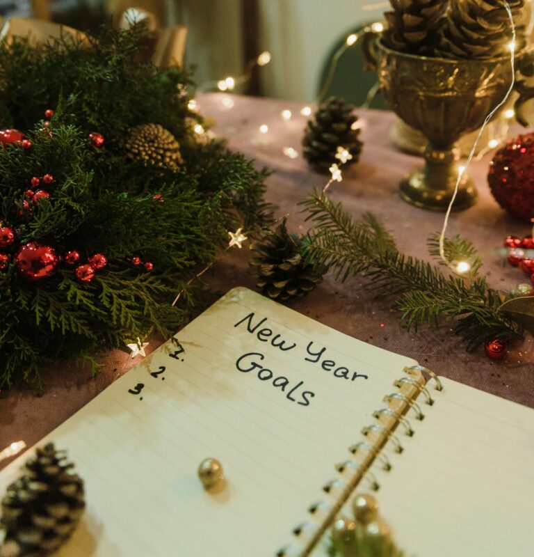 Notebook with New Year goals surrounded by festive Christmas decorations and lights.