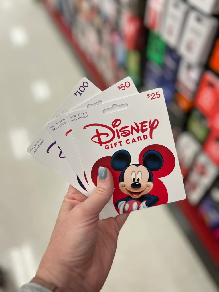 A hand holds three disney gift cards in different denominations. 