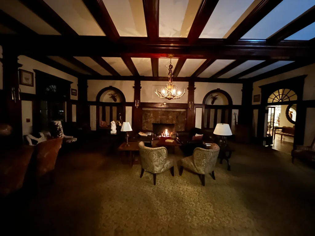 A room with wood beams on the ceilings and wood trim around the room. A fireplace is centered on the back wall.
