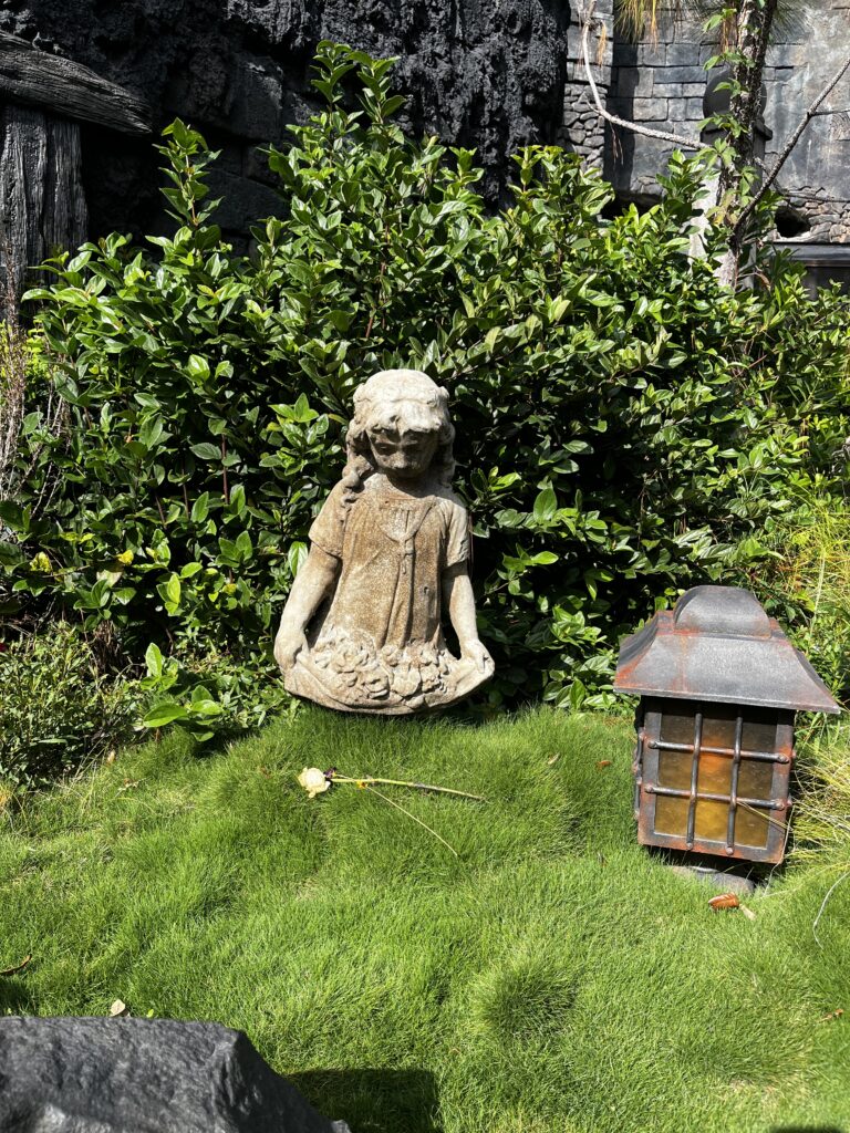A statue of a girl with flowers cupped in her dress sits in a garden