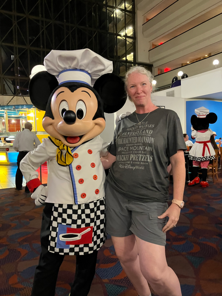 A woman stands with a Mickey Mouse character that is dressed as a chef.