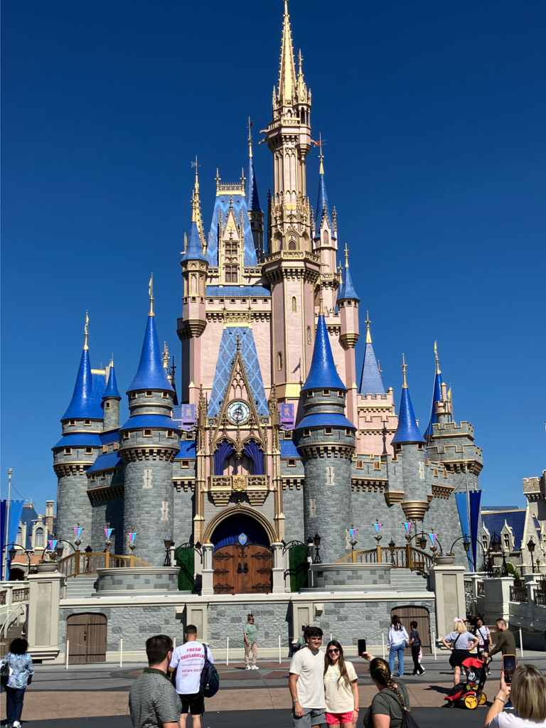 Cinderella's castle with pink walls and blue roofing, is backdropped by a clear blue sky.