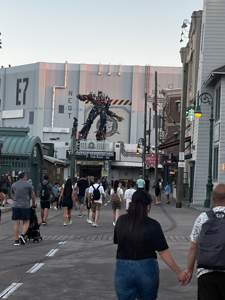 A crowd of people walk toward a building with a Optimus Prime statue above the entryway.