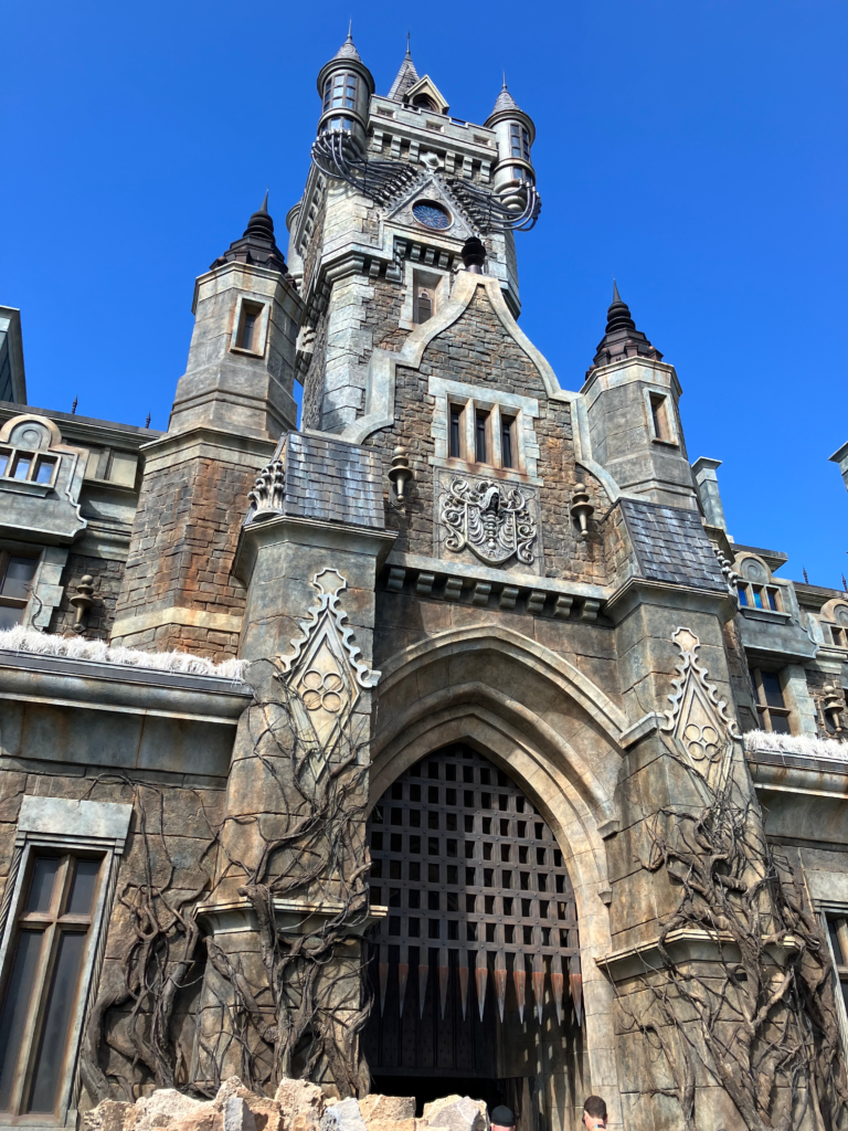 The entry to a tall gothic style castle against a blue sky.