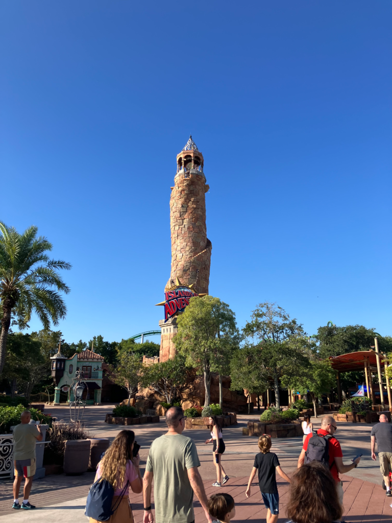 A bell tower stands above palm trees as guests walk to the entrance of Islands of Adventure theme park.