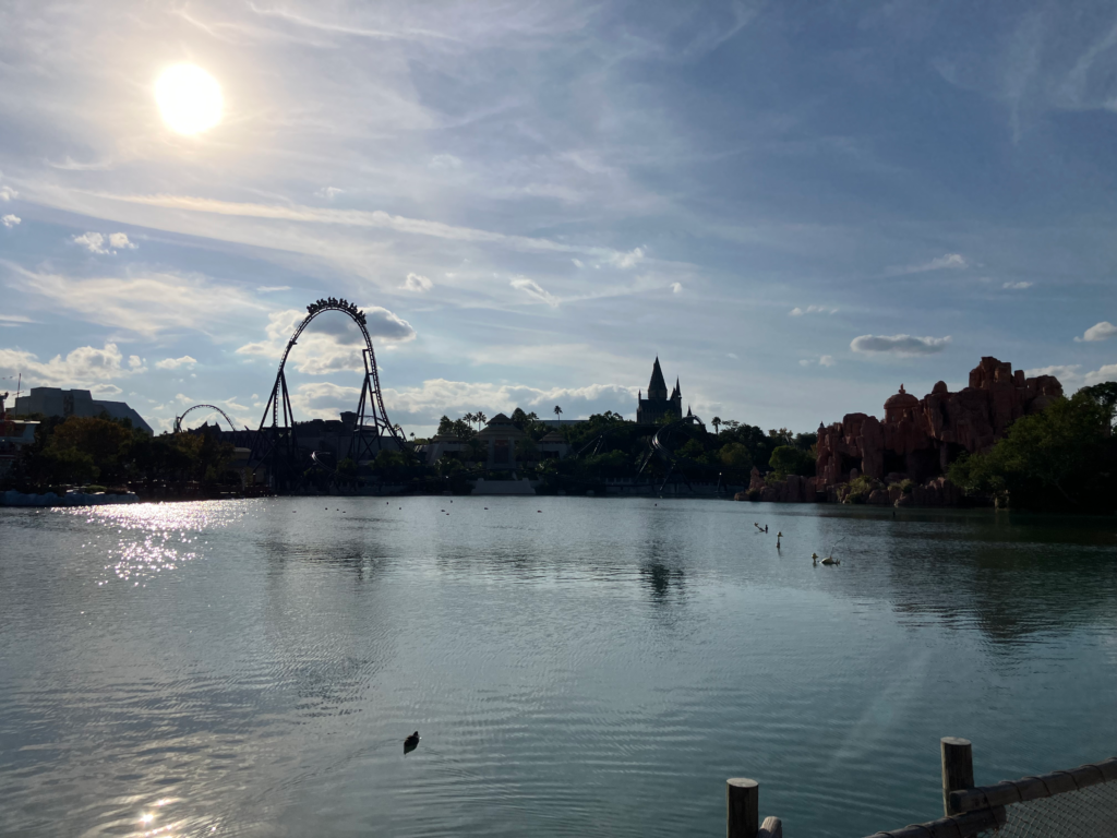 A rsilhouette of a oller coaster vehicle can be seen on the apex of the track beyond a lake.