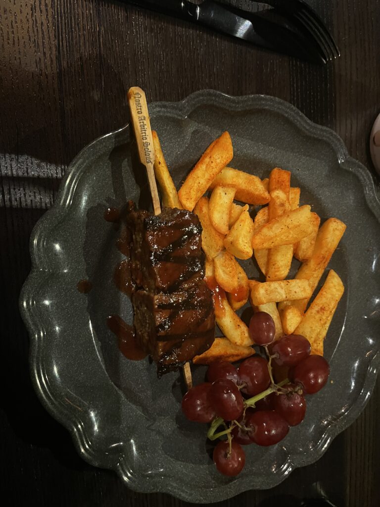 A plate of meatload on wooden skewers with grapes and french fries on the side.