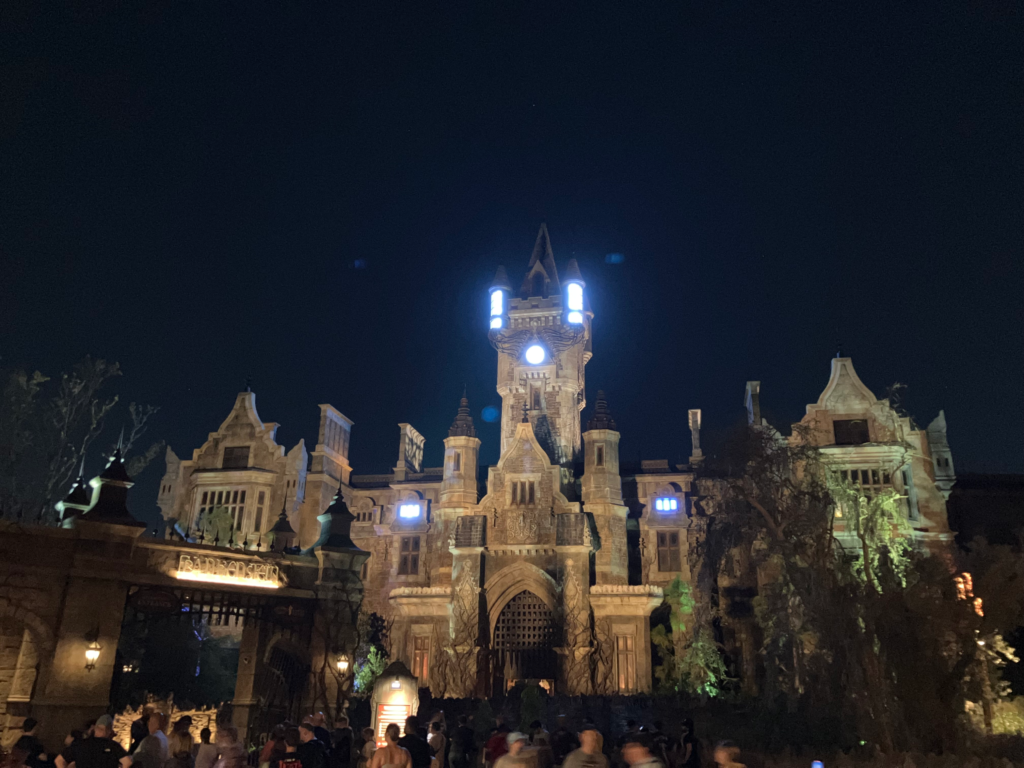 A gothic-style manor's windows glow purple with electrical energy against a dark night sky.