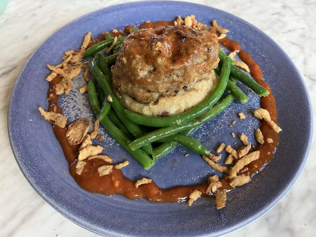 A skull-shaped meatloaf sits on mased potatoes encircled by green beans.