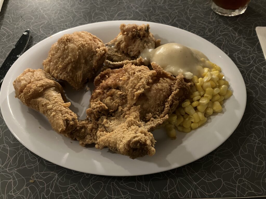 Three large pieces of fried chicken on a plate with corn, mashed potatoes and gravy.