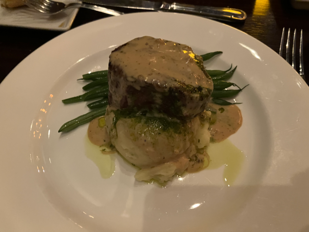 A thick cut of filet minion sits on a mound of mashed potatoes and some green beans.